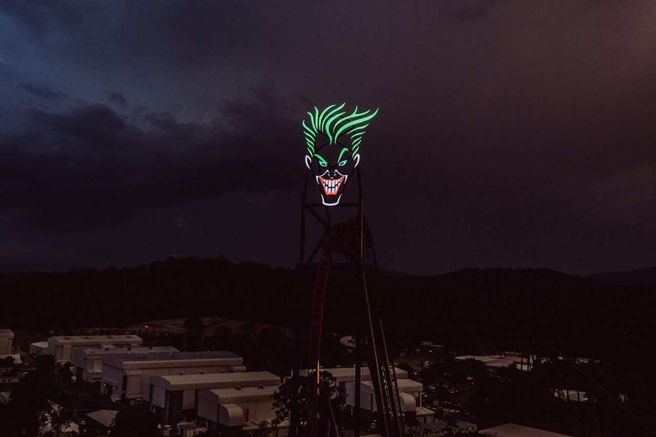 Illuminated Joker face above the DC Rivals ride at Movie World at night.