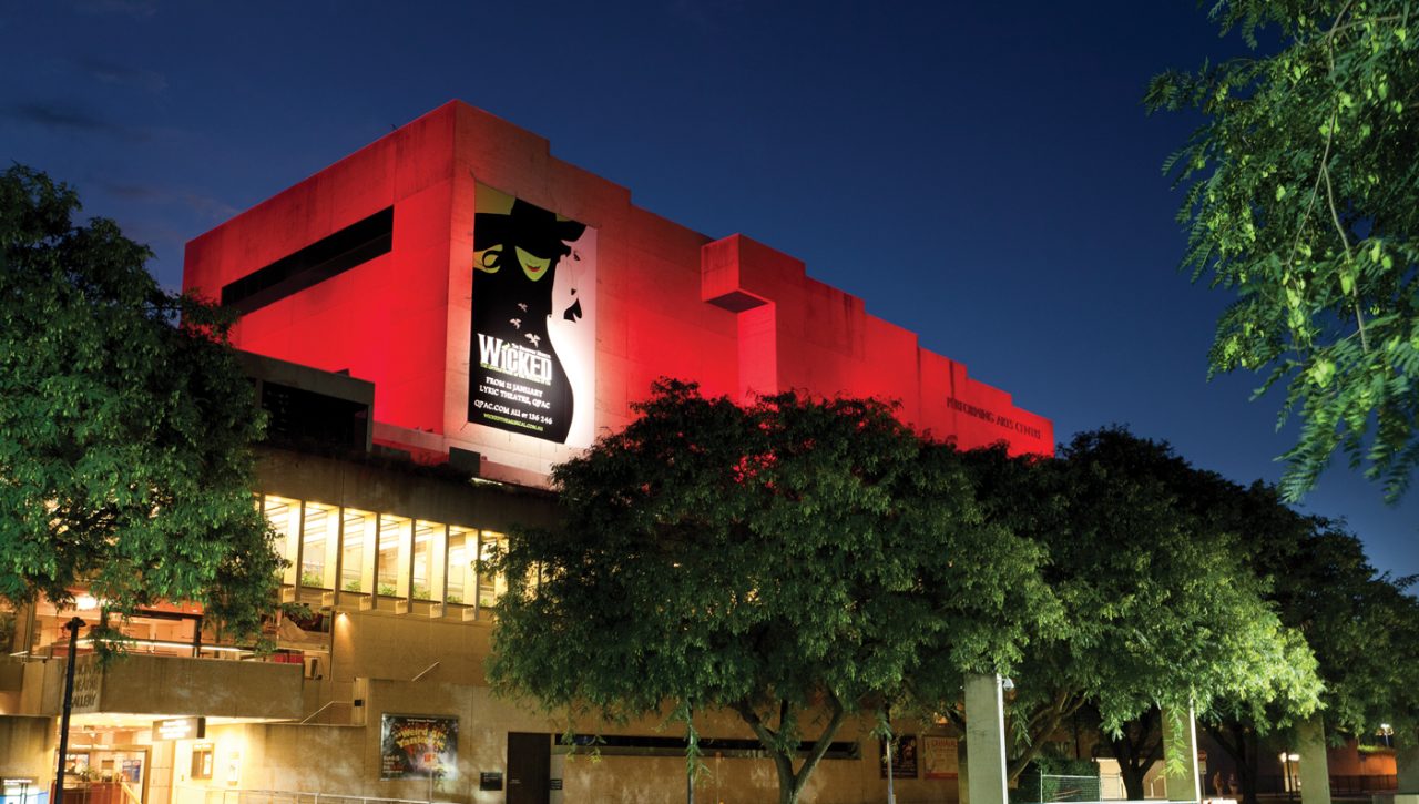 Red lighting across the QPAC facade above trees at night.