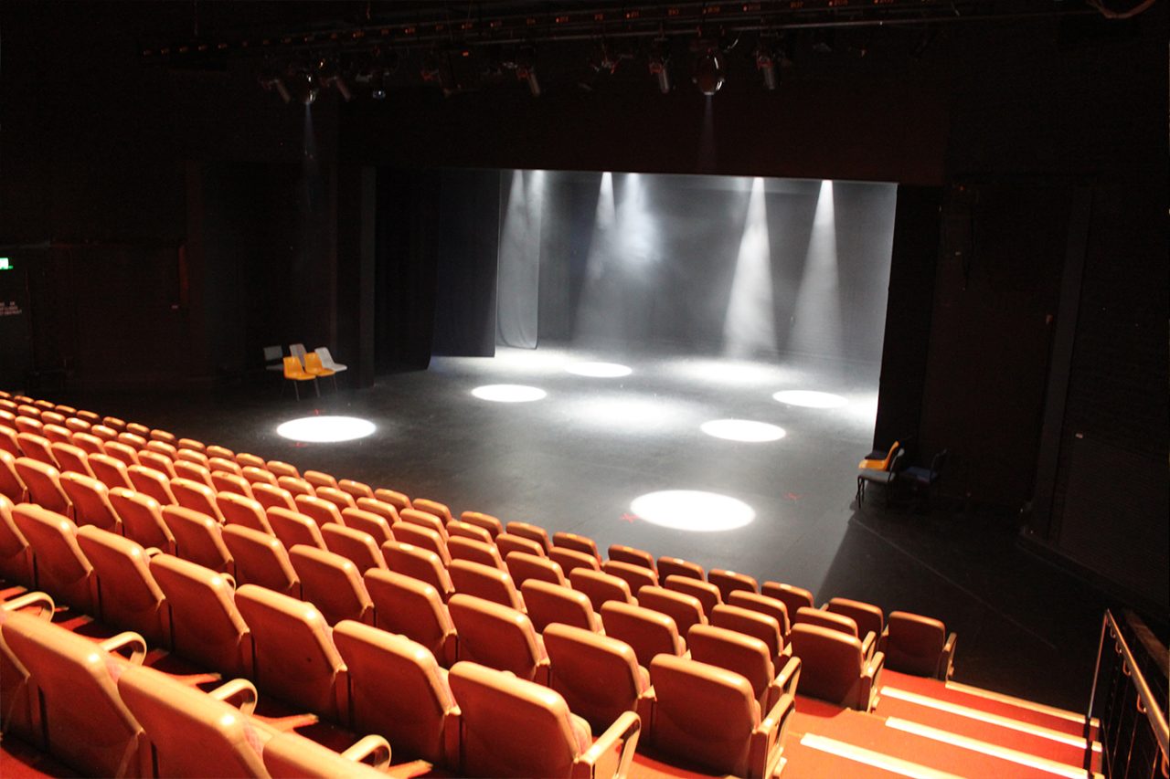 White spotlights on an empty stage beside rows of theatre seats at WAAPA.