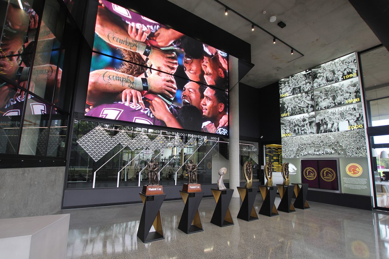 Large video screen above trophy displays in the Brisbane Broncos Leagues Club foyer.