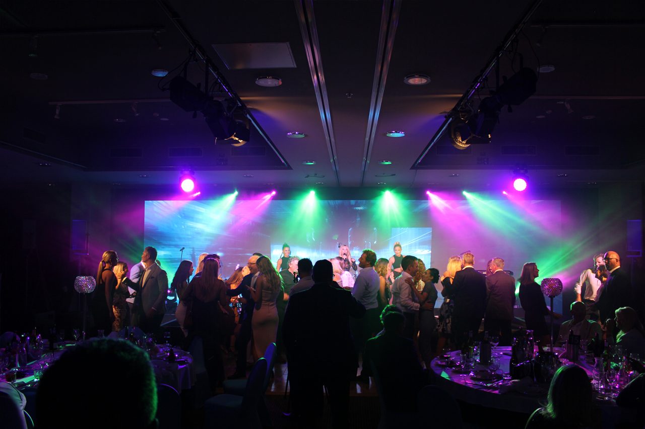 Gala guests dancing beneath purple, green and blue stage lights.