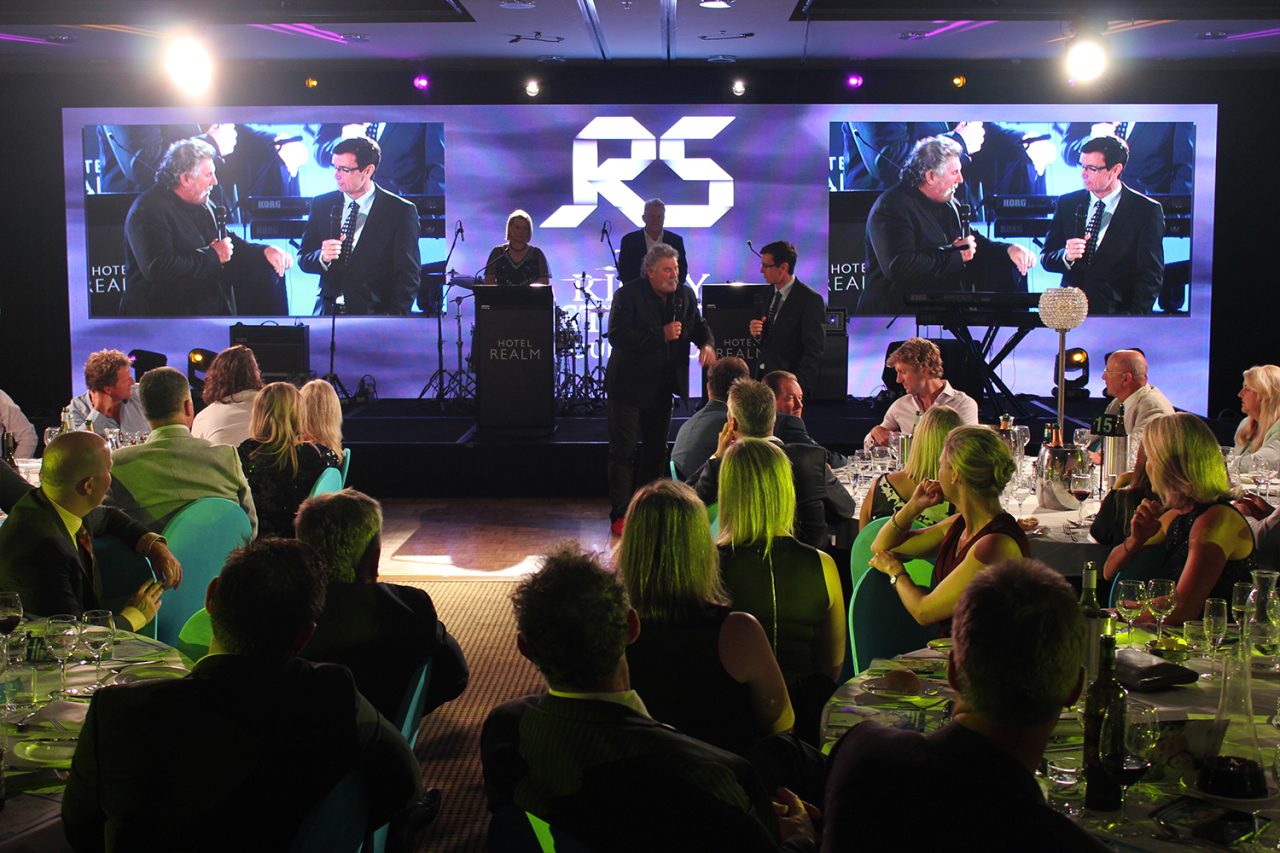Speakers onstage with live camera images displayed on two LED screens.