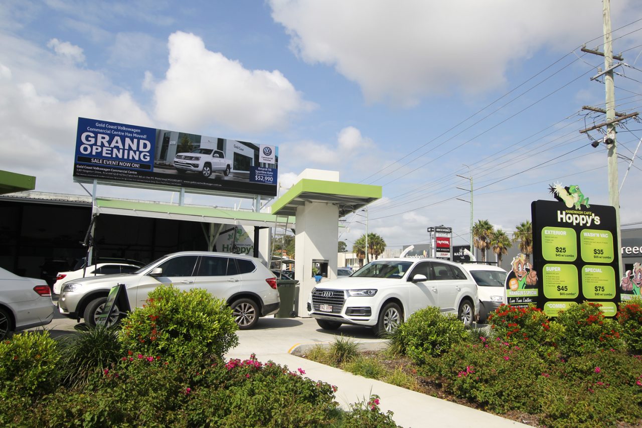 Cars outside Hoppy's Handwash Cafe beneath a rooftop digital advertisement.