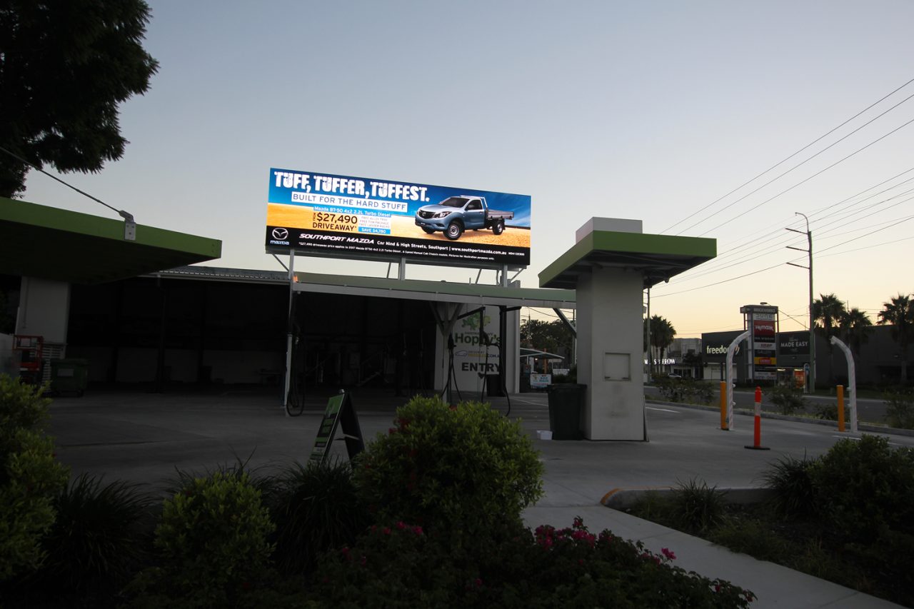 Illuminated Hoppy's digital billboard beside the road at dusk.