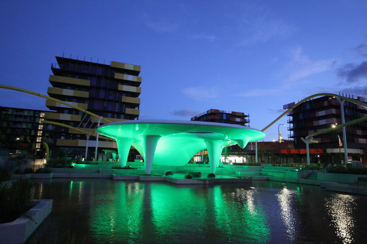 Green-lit pavilion reflected in the water at the 2018 Commonwealth Games Village.