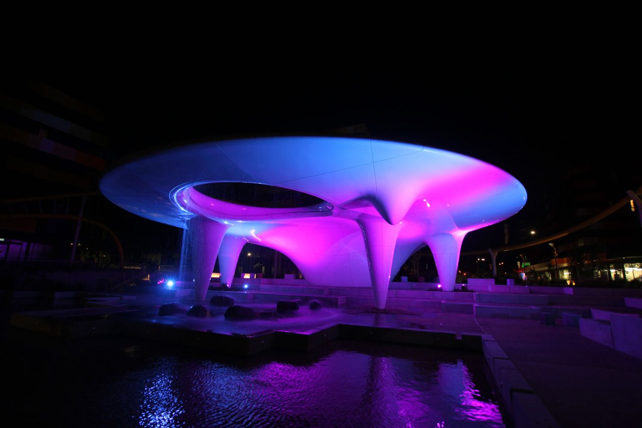 Purple and blue lighting beneath the curved village pavilion canopy.