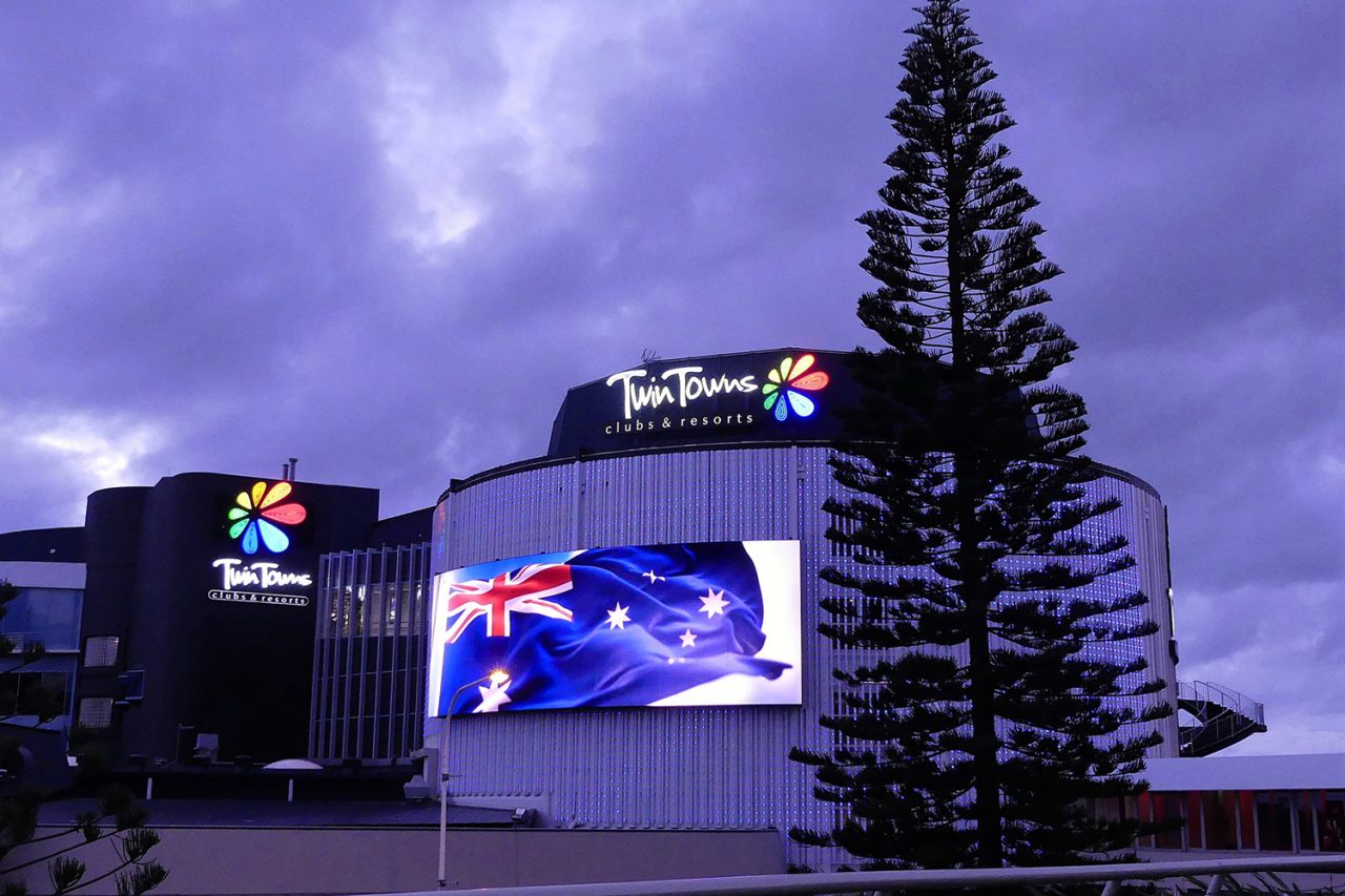 Blue and white video imagery on the Twin Towns facade beneath a purple dusk sky.