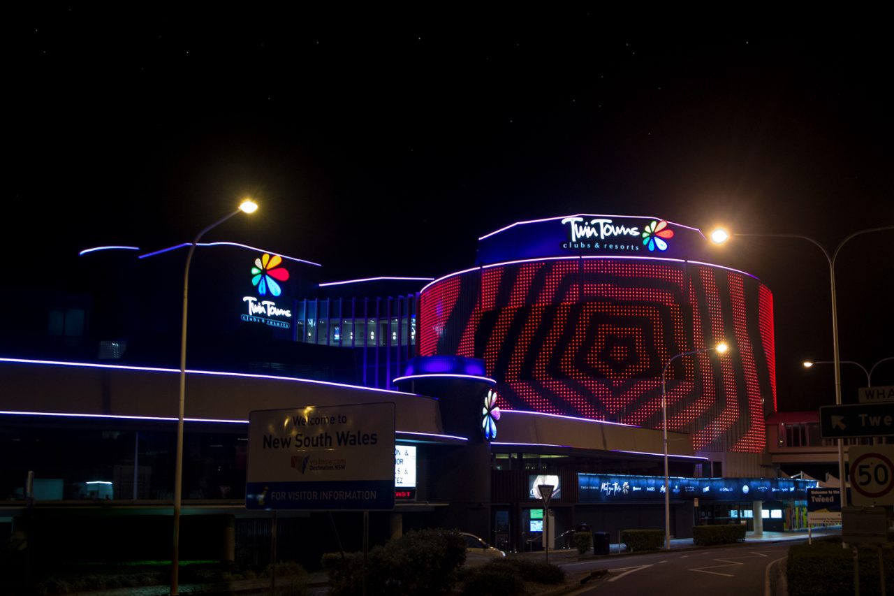 Red patterns across the Twin Towns digital facade beside the road at night.