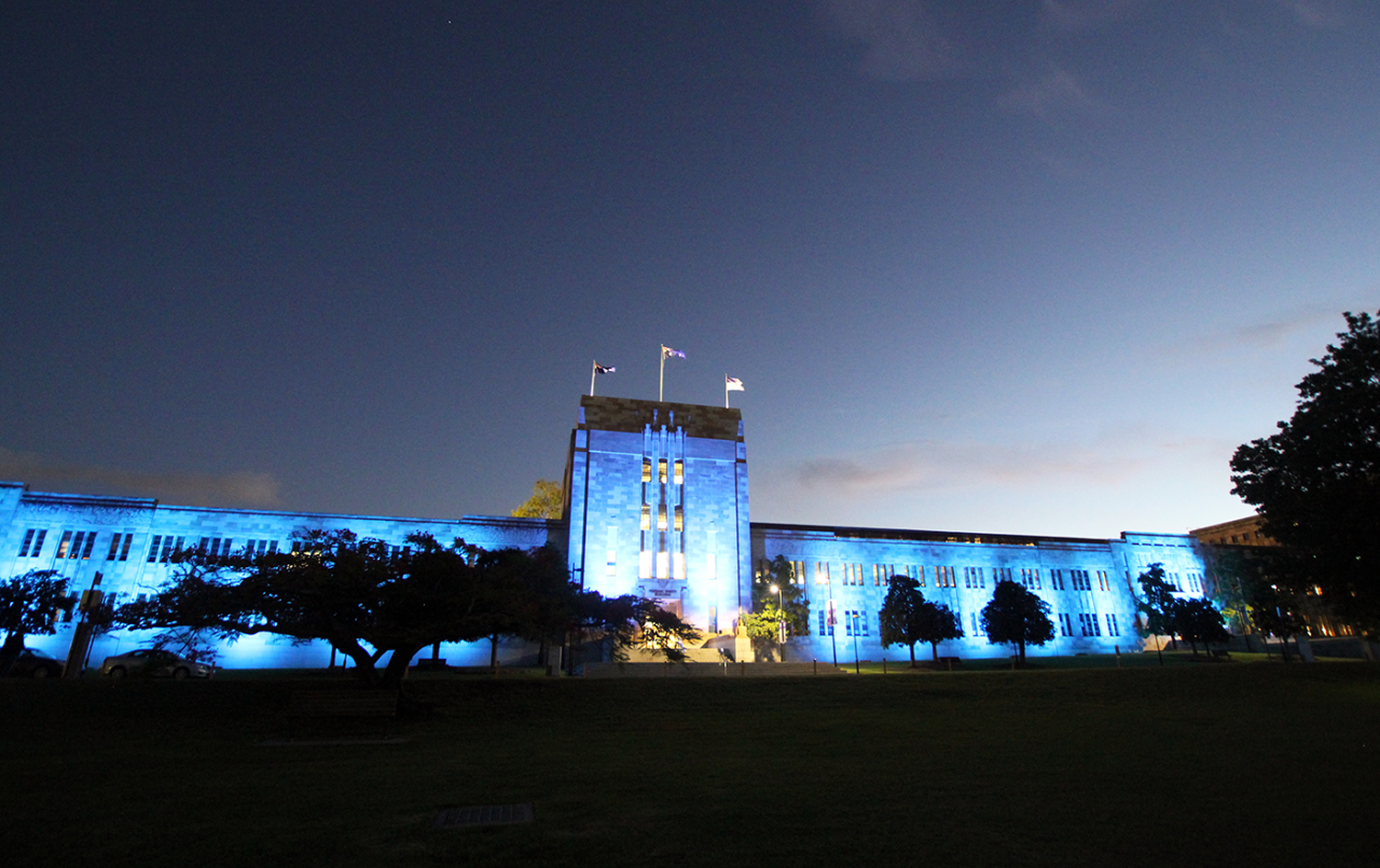 Wide view of the blue-lit Forgan Smith Building at dusk.