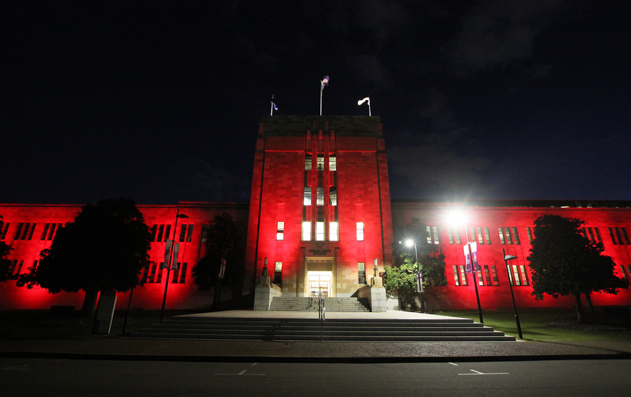 Red lighting across the Forgan Smith Building and central tower at night.