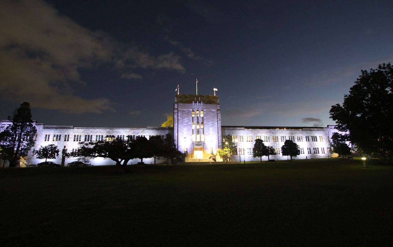 White illumination across the Forgan Smith Building beneath a cloudy night sky.