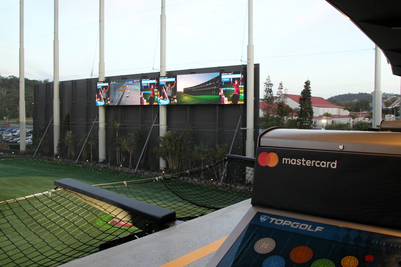 View from a Topgolf bay toward the driving range and distant LED screens.