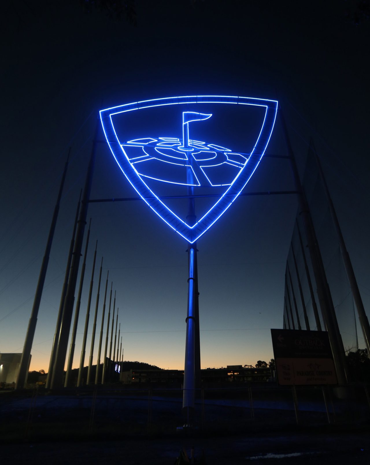 Tall Topgolf sign glowing blue against the dusk sky.