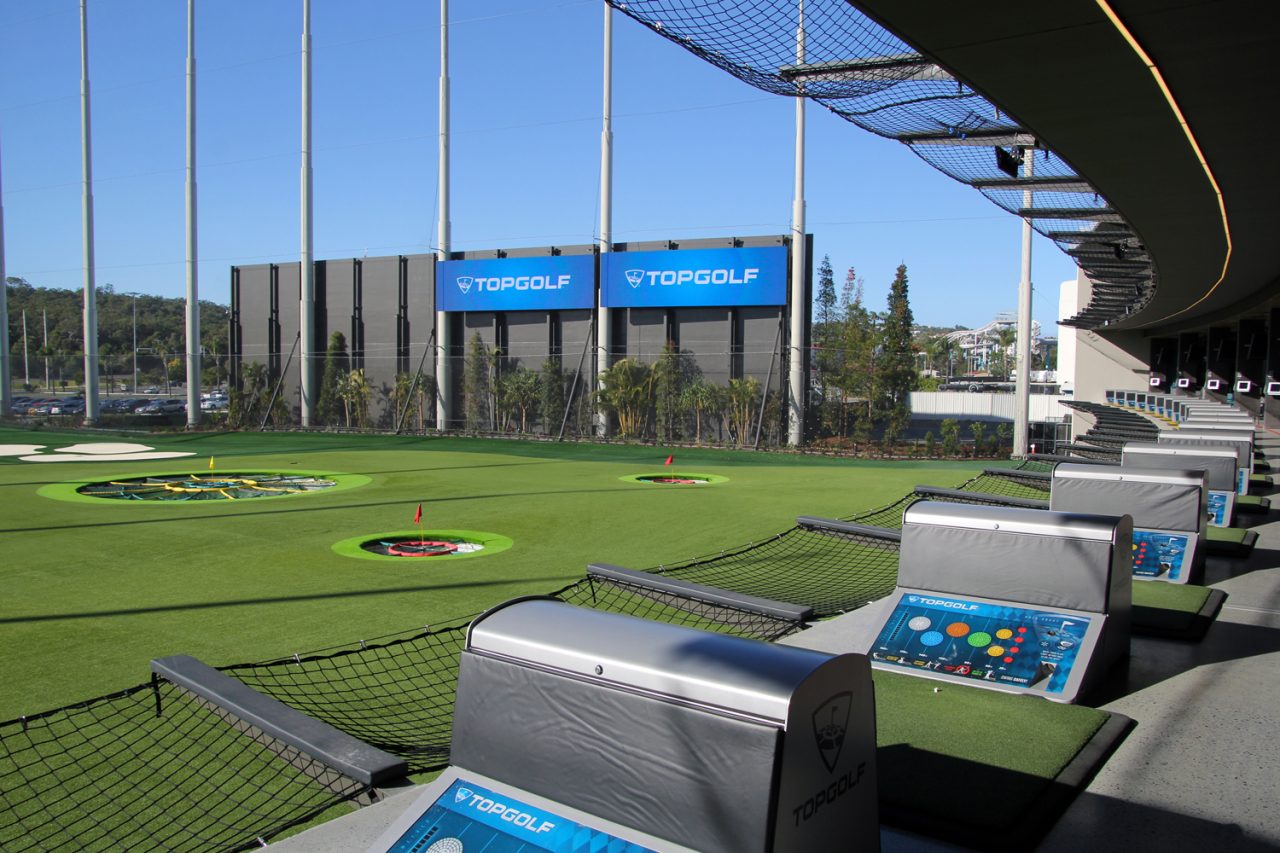 Two large Topgolf screens beyond the driving-range targets in daylight.