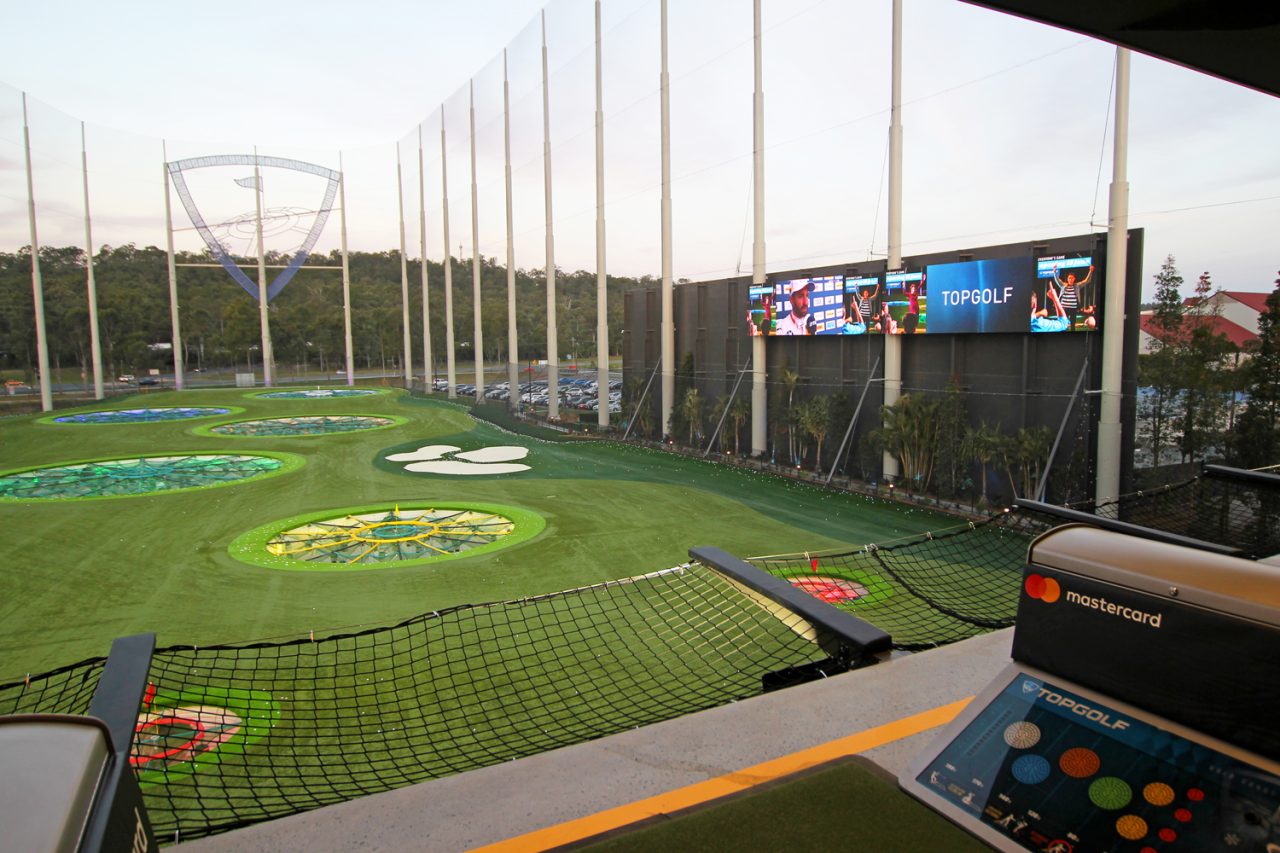 Video screens above the Topgolf targets viewed from a hitting bay in the evening.