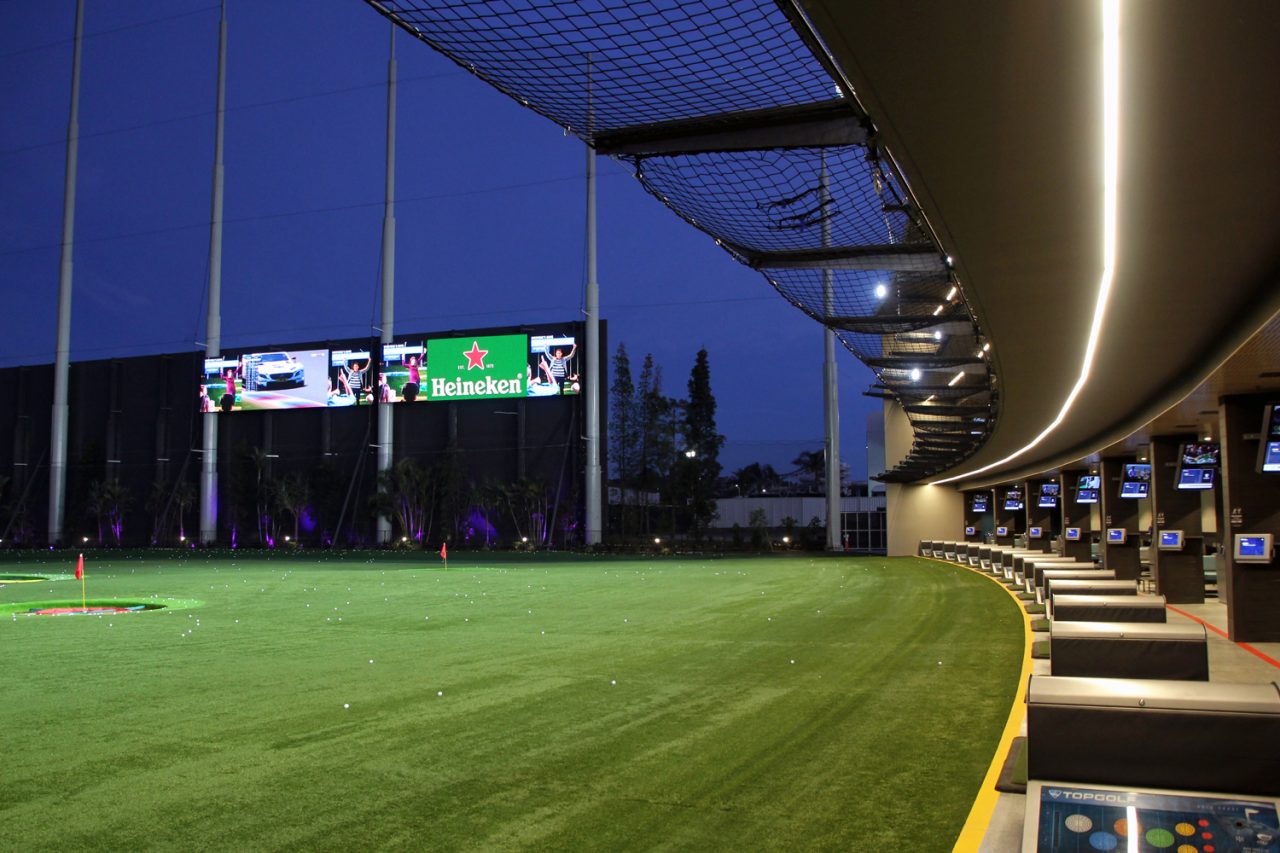 Illuminated driving range and large video screens at Topgolf at night.