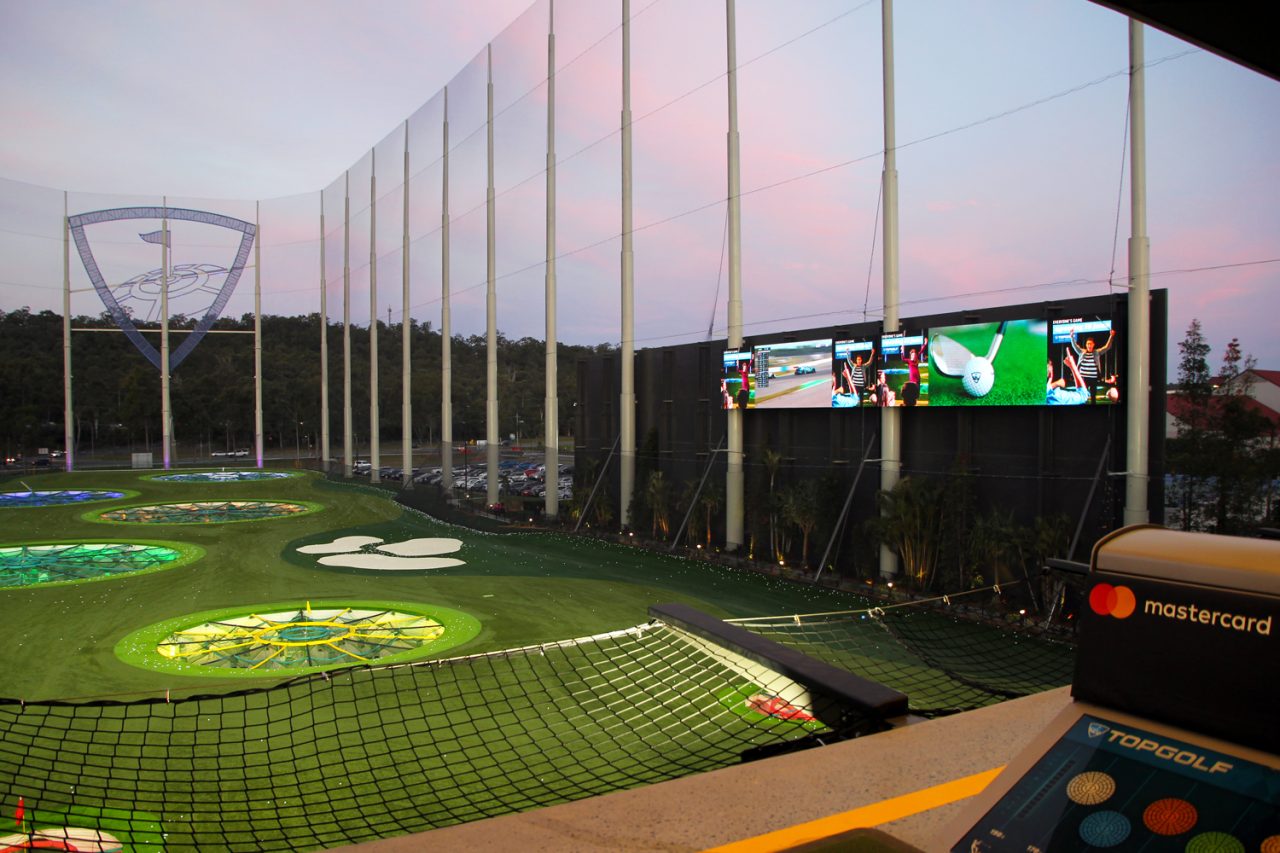 Sports footage on the large Topgolf screens at dusk.