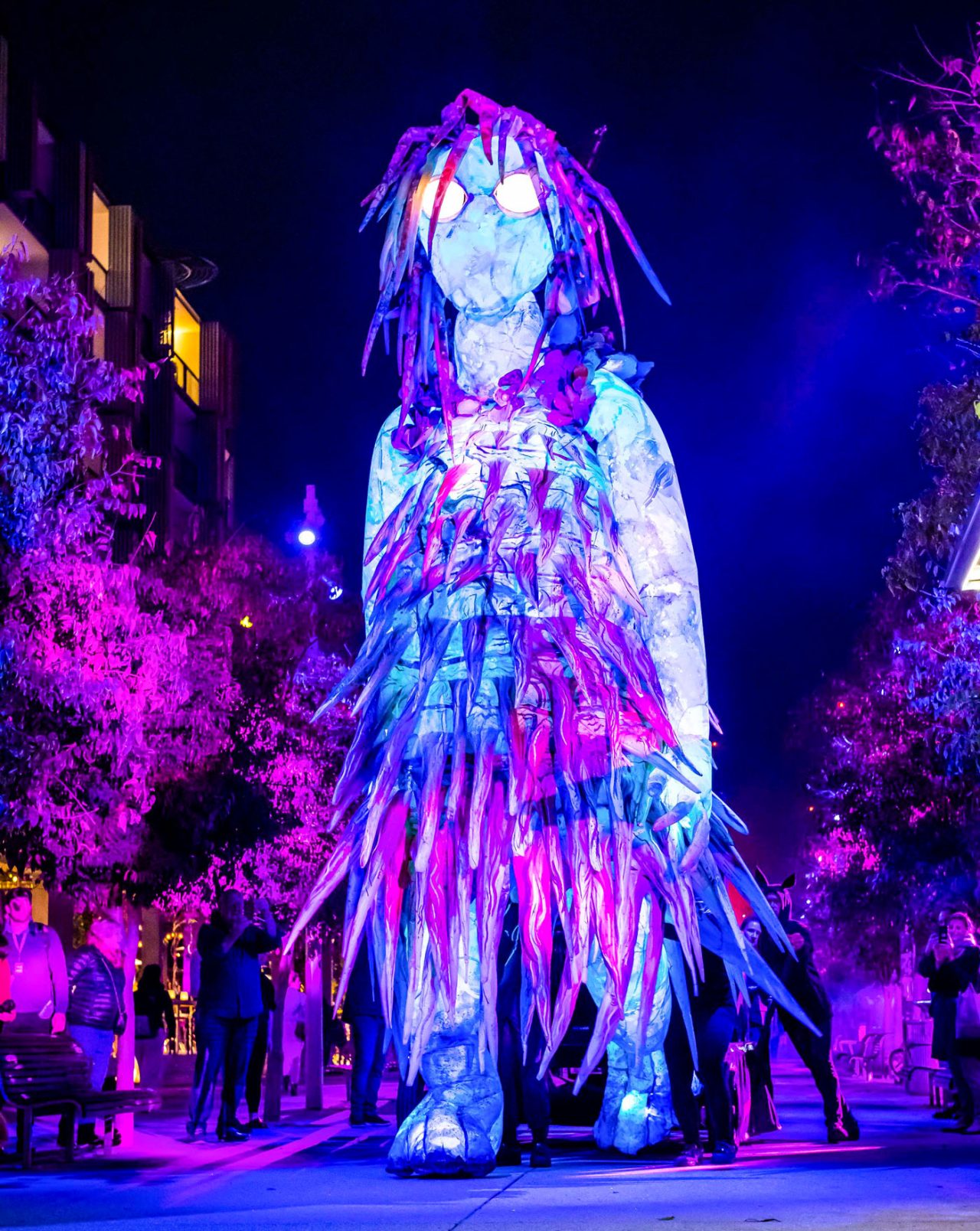 Tall blue and purple illuminated figure among trees at Vivid Sydney.