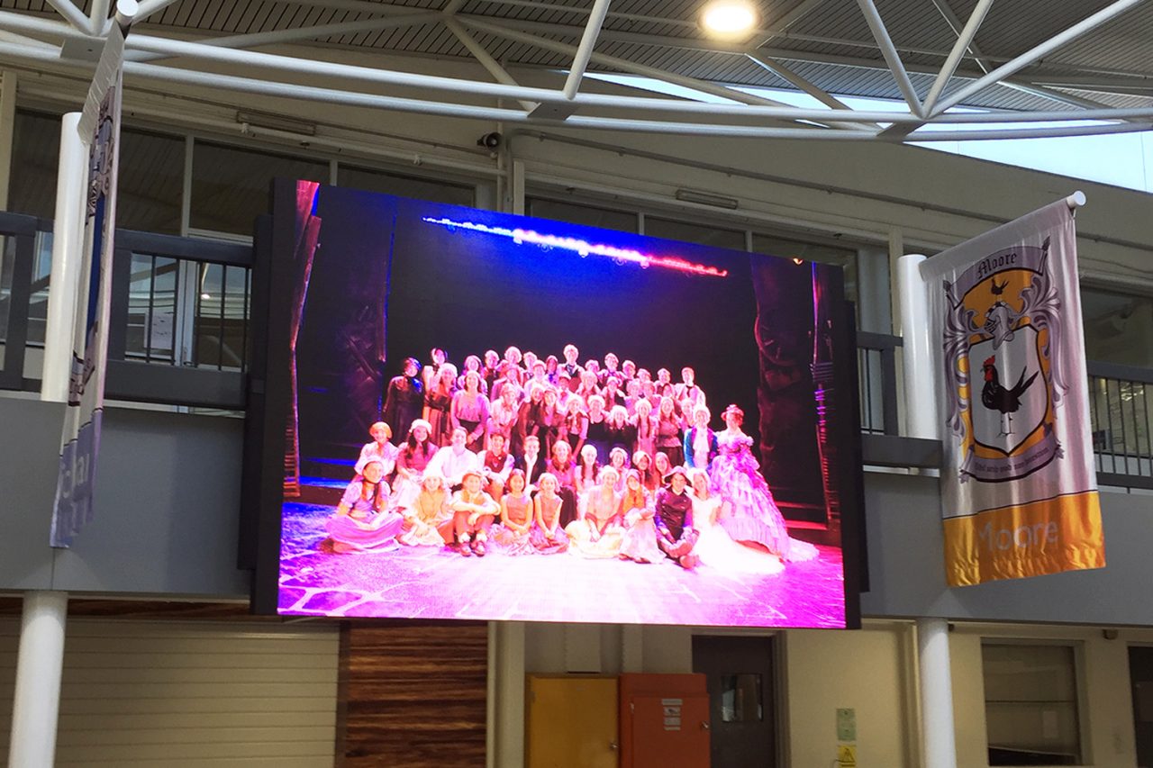 Carey Baptist Grammar display showing performers gathered on a pink-lit stage.