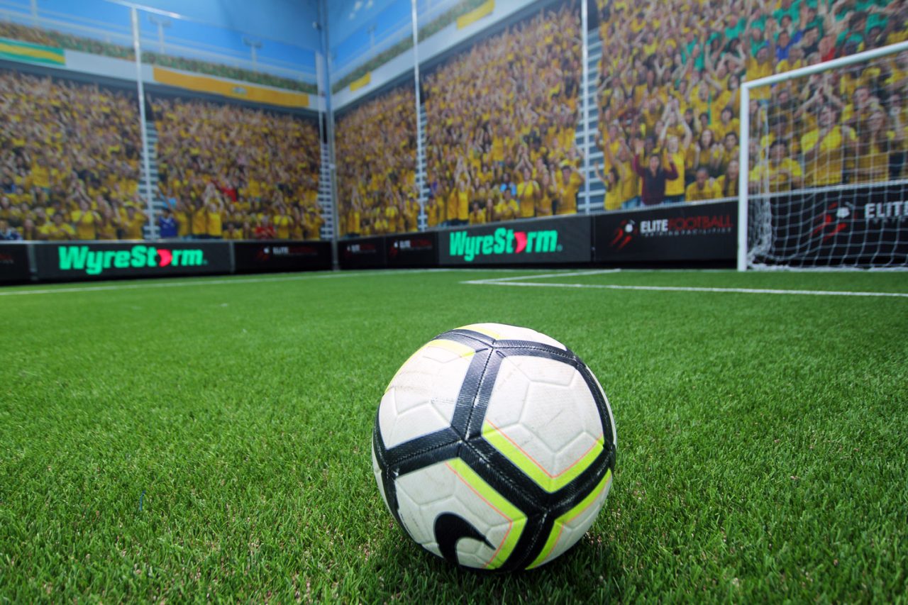 Football on indoor turf in front of stadium imagery on the surrounding walls.
