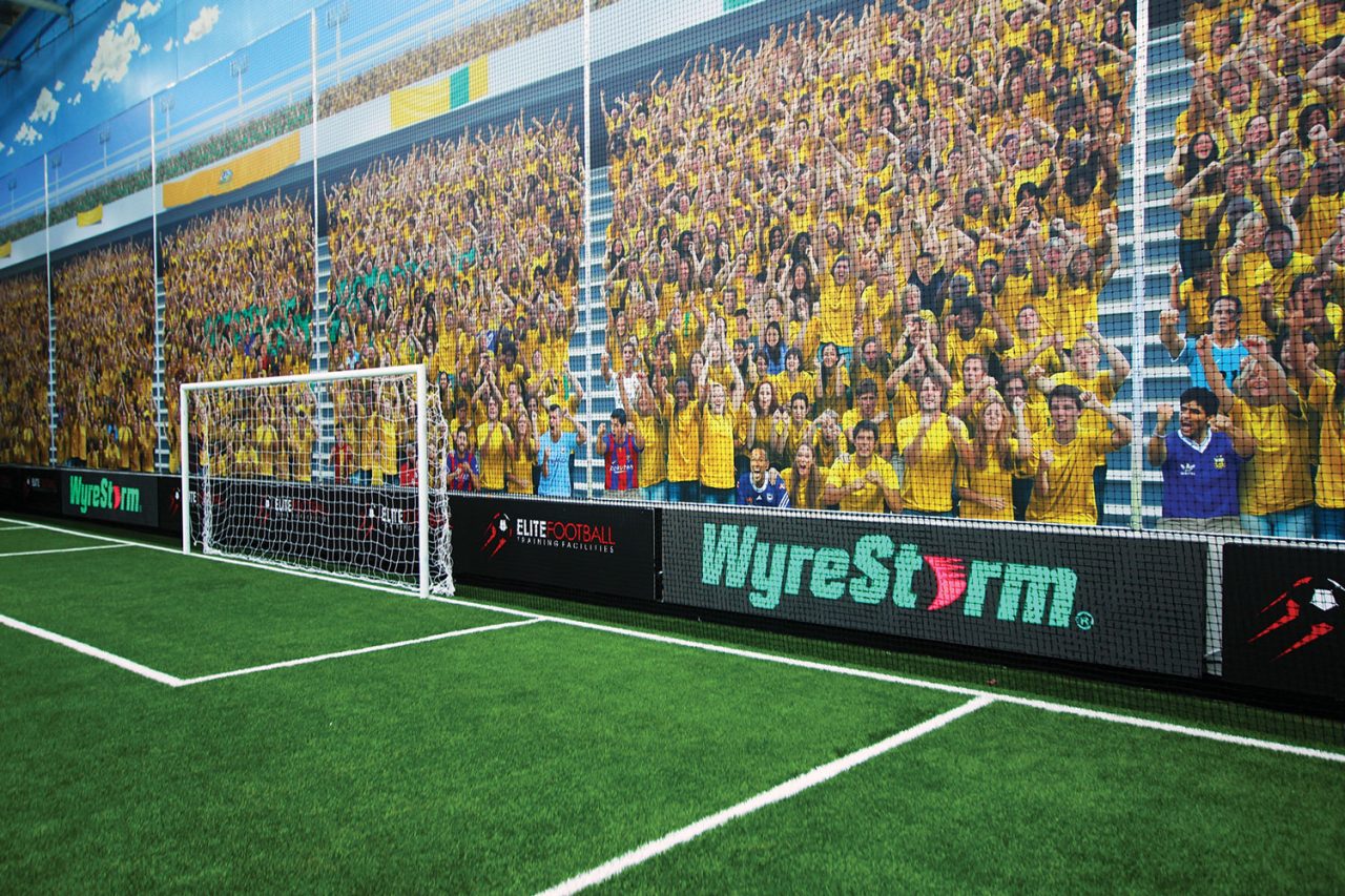 Indoor football goal beside a digital advertising ribbon and stadium mural.