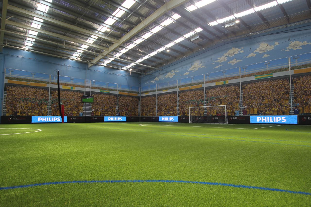 Indoor football pitch with digital screens along the surrounding walls.