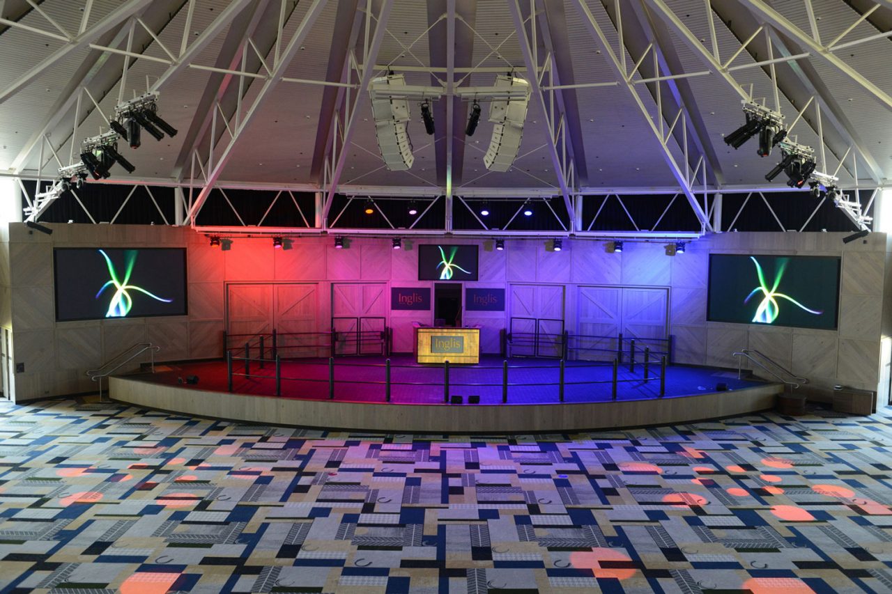 Empty auction stage and paired video screens beneath coloured lighting at Inglis Riverside Stables.