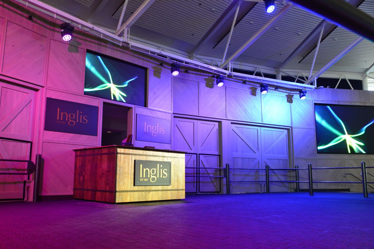 Inglis podium between screens and purple-lit wall panels at Riverside Stables.