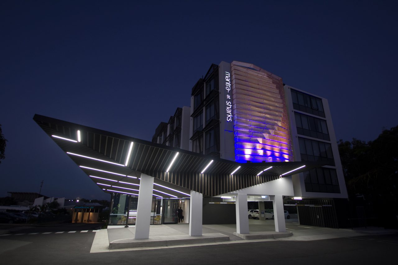 Illuminated entrance canopy and facade artwork at Mantra at Sharks at night.