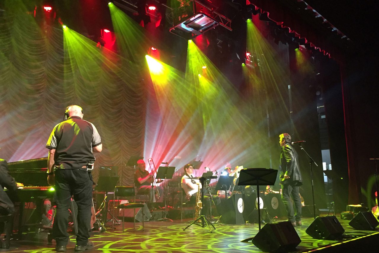 Side view of musicians beneath red and green beams at Ipswich Civic Centre.
