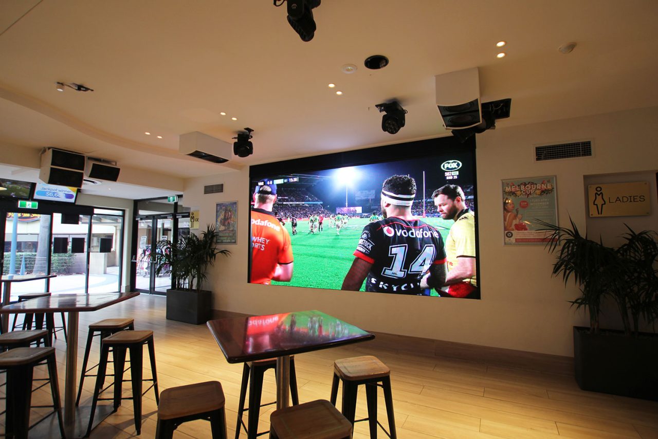 Sports footage on the large screen above tables at Melbas on the Park.