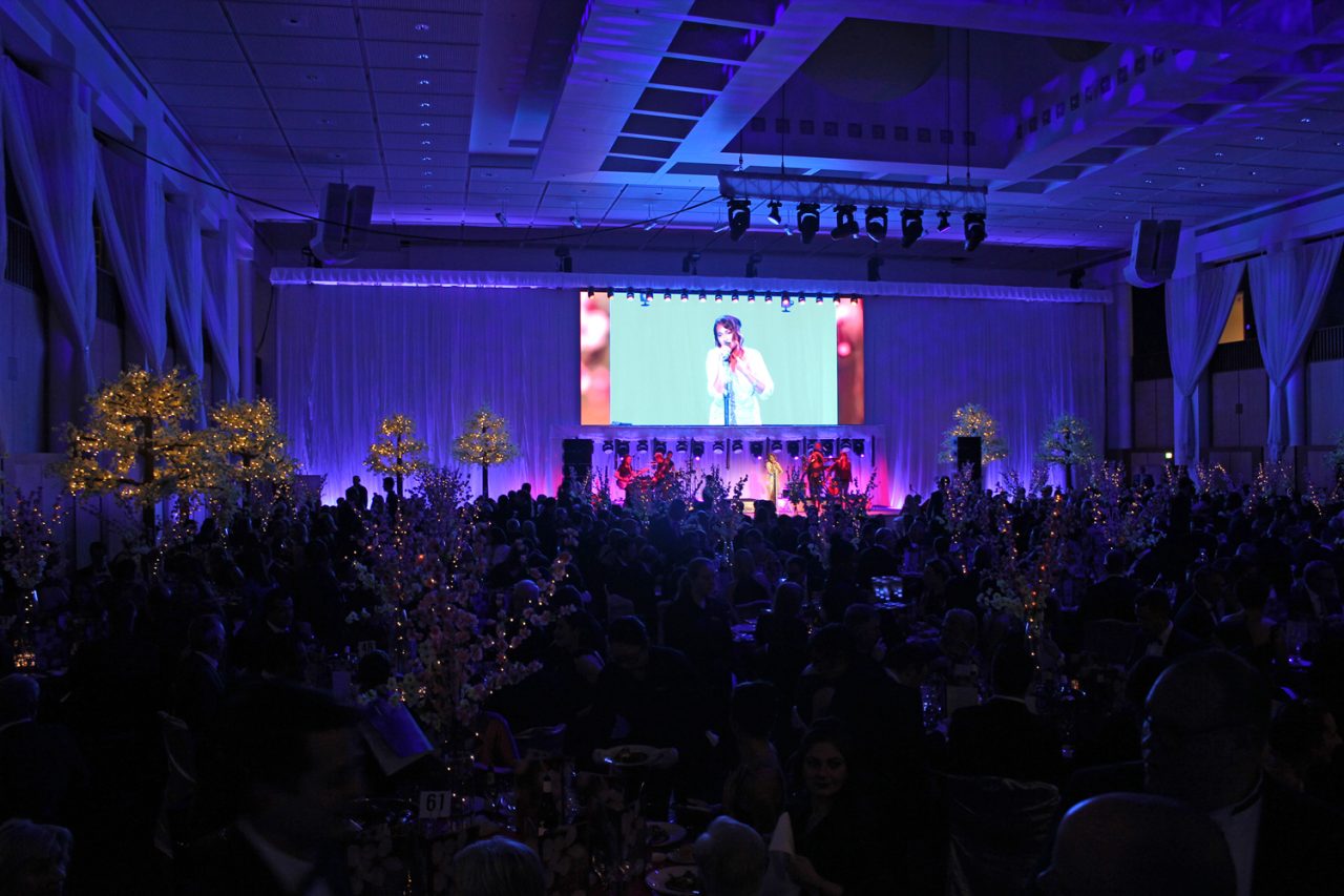 Blue-lit hall with video footage on the central screen at the Mid Winter Ball.