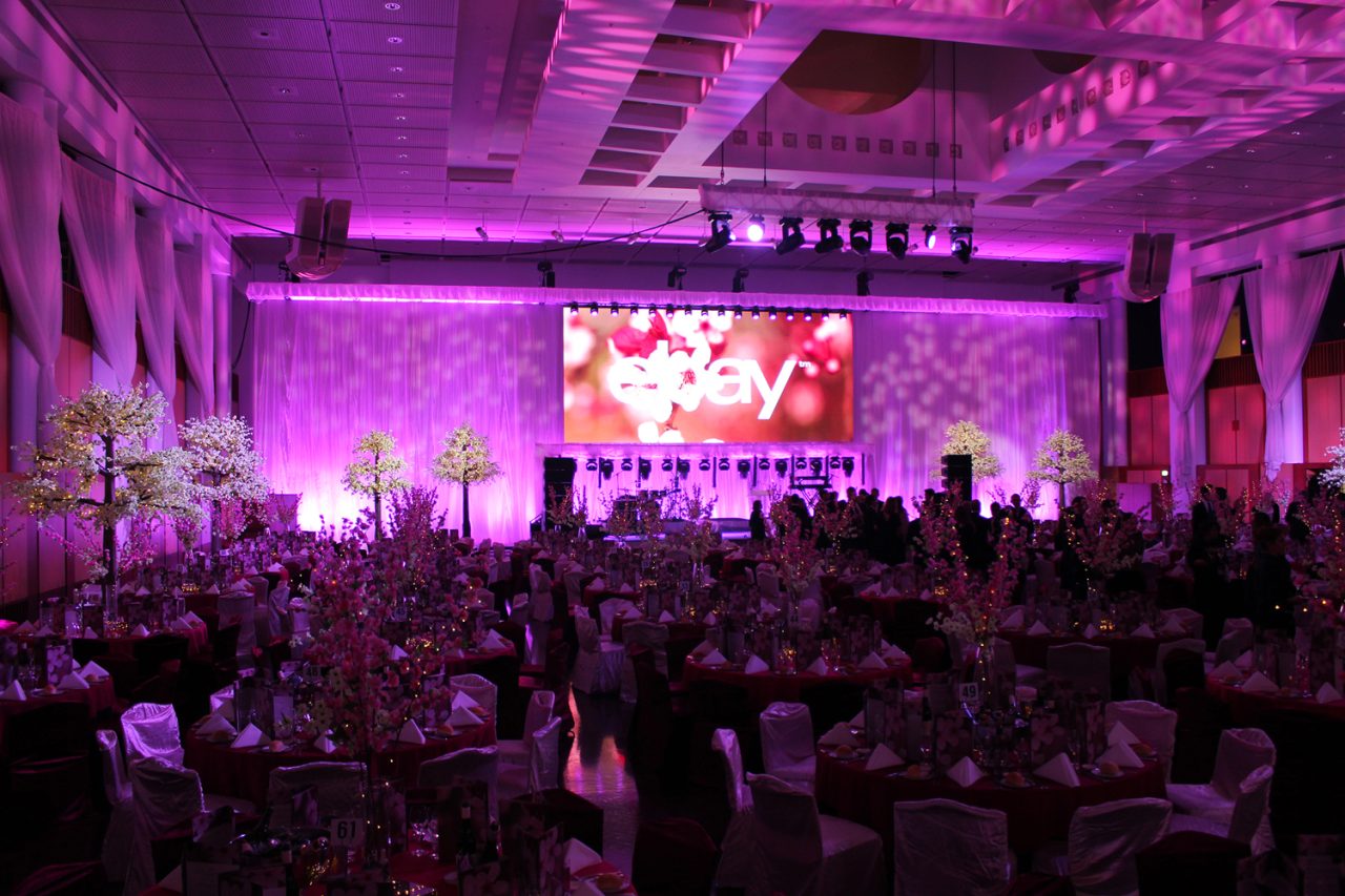 Purple lighting over banquet tables and the large stage screen at the Mid Winter Ball.