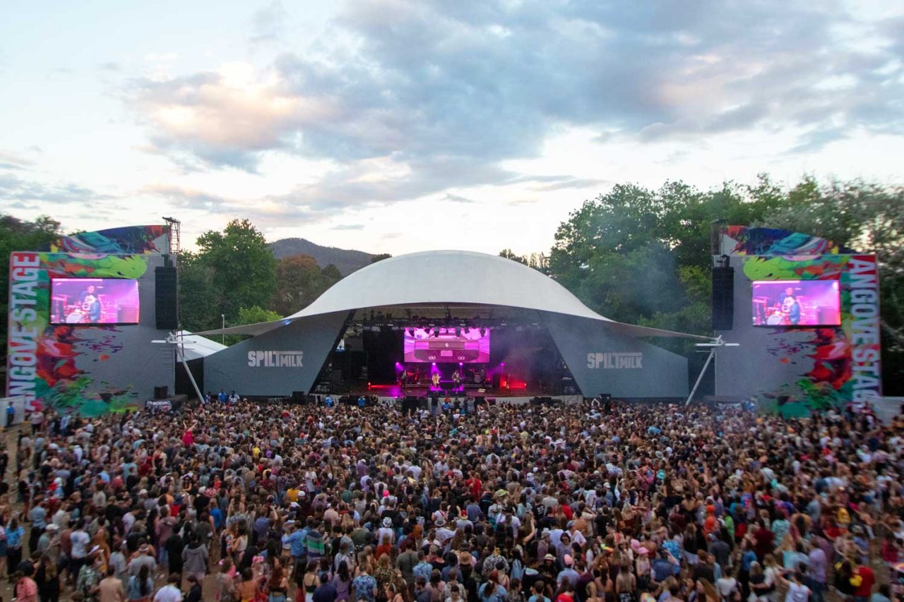 Large festival crowd facing the curved main-stage roof and side screens at Spilt Milk 2018.