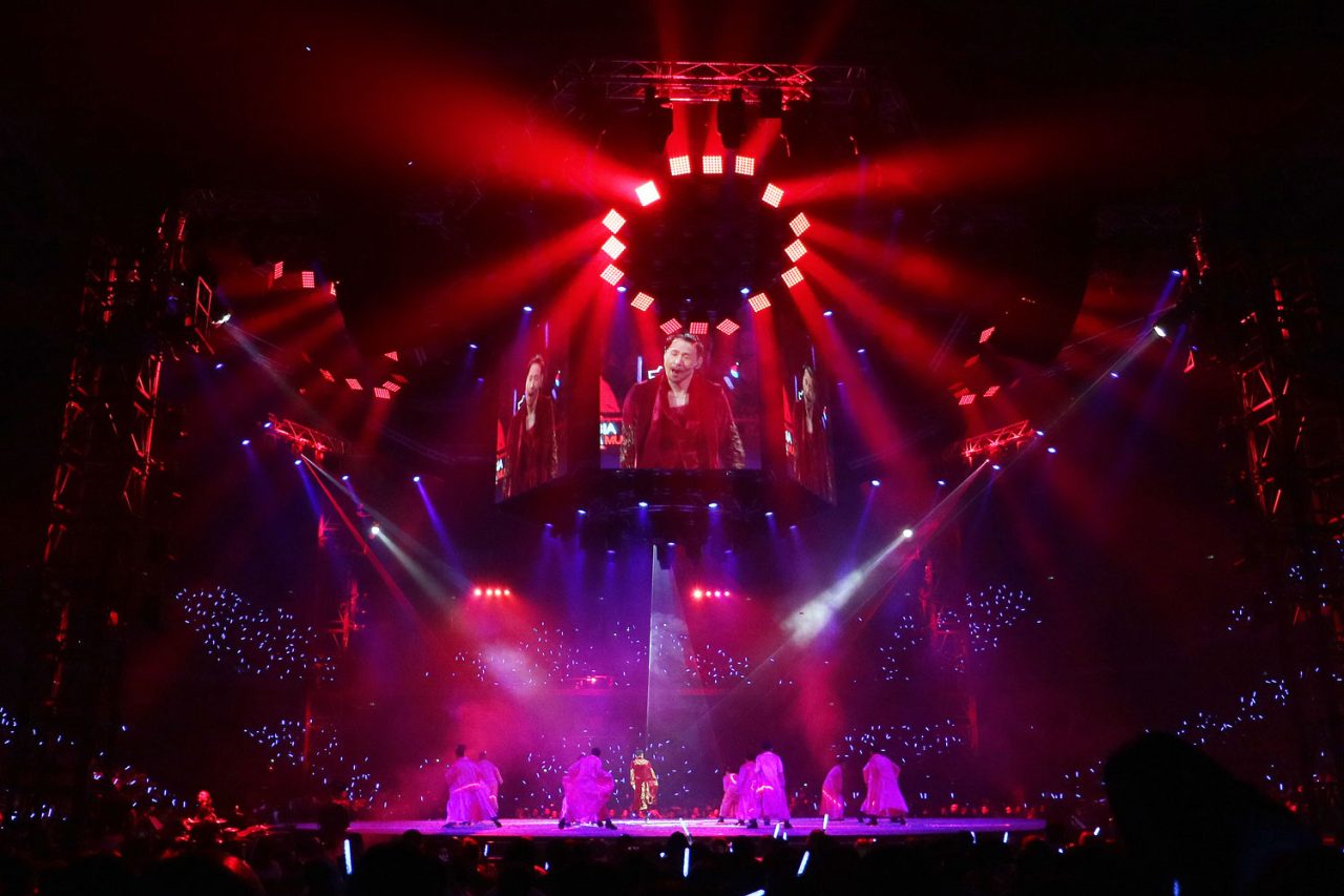 Red lights radiating from an overhead circular rig during Jacky Cheung's show.