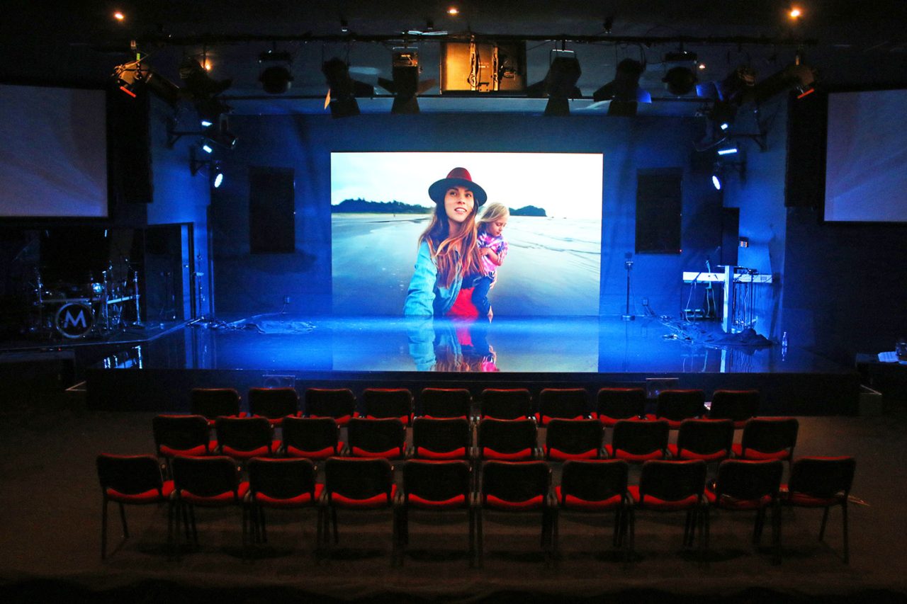 Large stage screen showing a performer above empty seating at Metro Church.