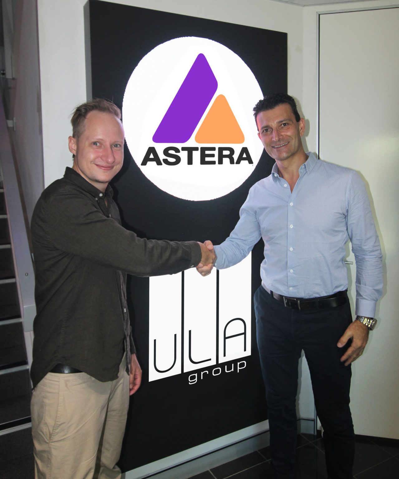 ULA Group and Astera representatives shaking hands beside their brand display.