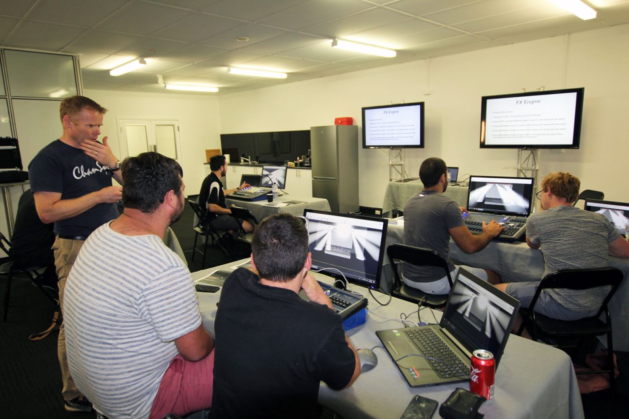 Trainer helping participants at lighting consoles in a classroom.