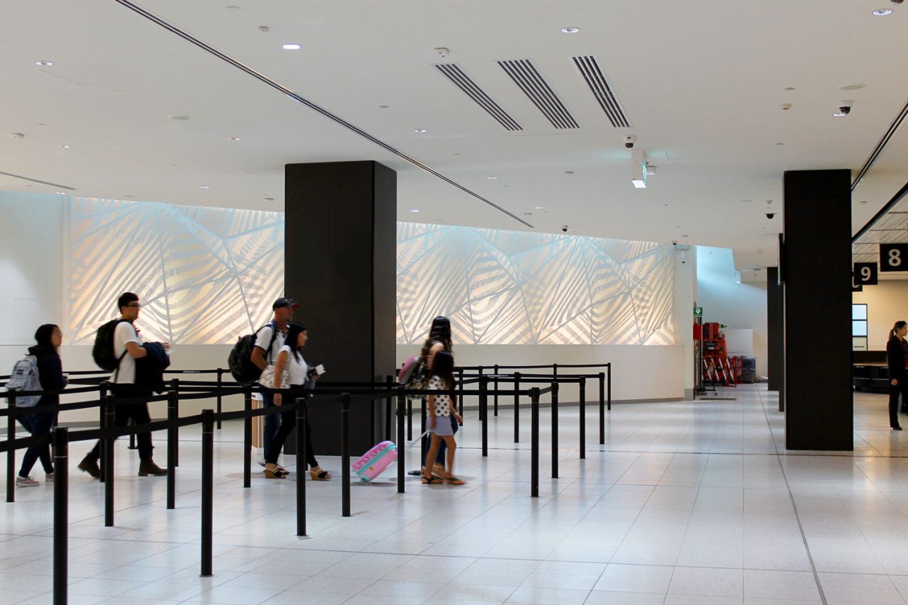 Passengers beside the illuminated Traverse artwork in an airport terminal.