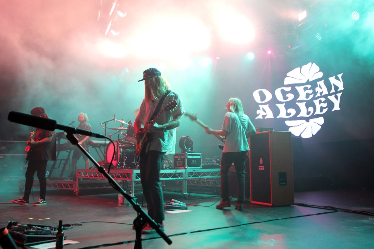 Ocean Alley performing under green and warm stage lighting.
