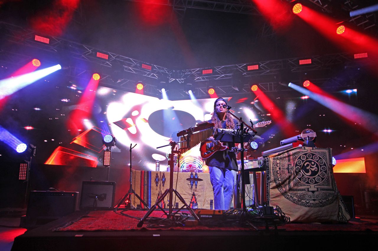 Tash Sultana performing amid red and white lighting on the Flow State tour.
