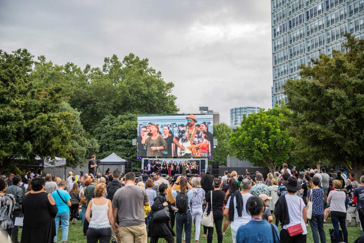 Audience gathered on the lawn facing the Auckland Live outdoor screen.