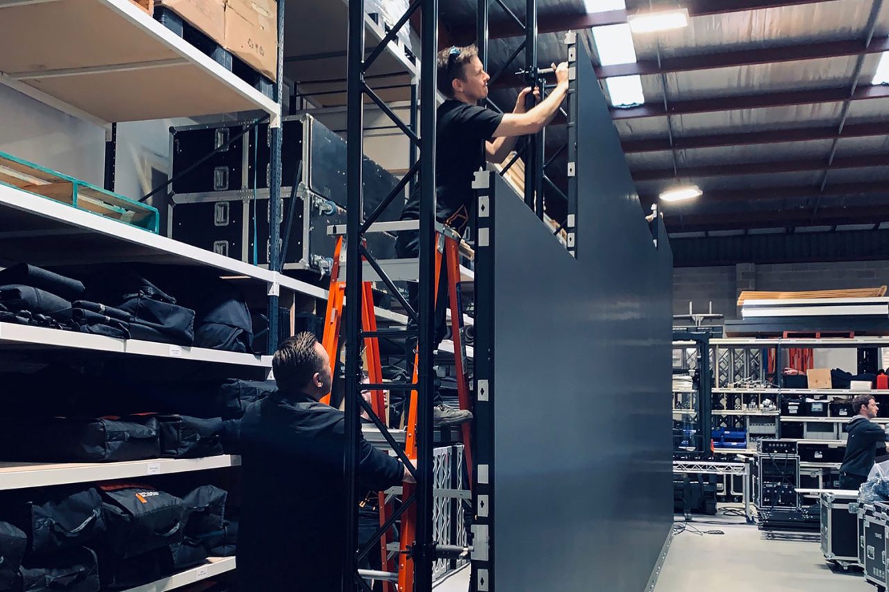 Technicians fitting LED panels to a tall screen frame in the warehouse.