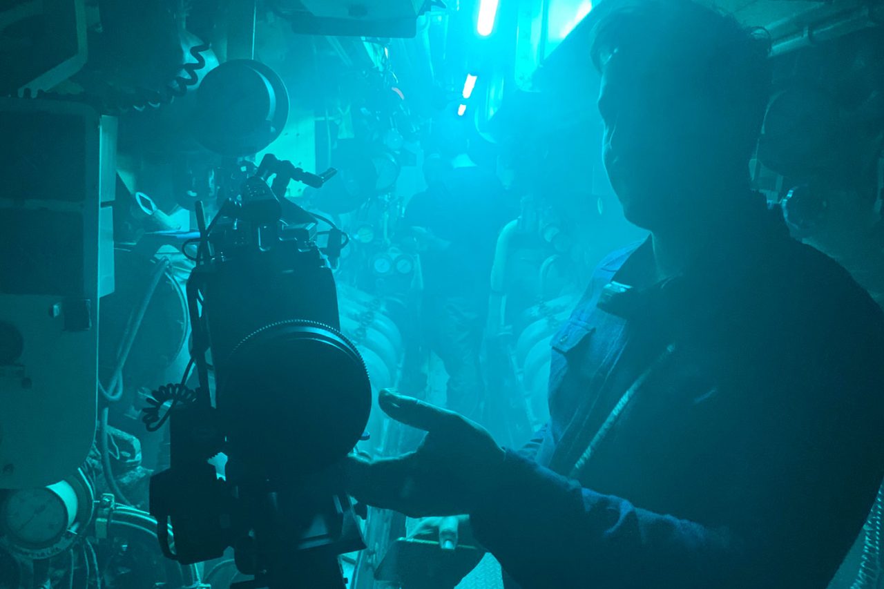 Camera operator silhouetted in blue light inside a submarine.