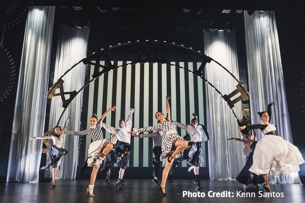 Dancers beneath a large mechanical arch in the HOTA production of Wicked.