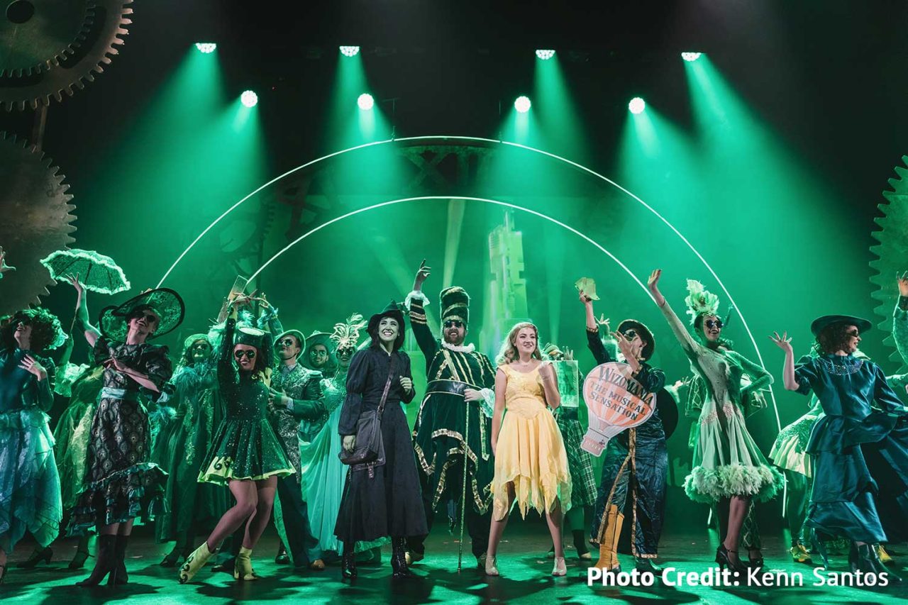 Wicked ensemble beneath green beams and curved scenic structures at HOTA.