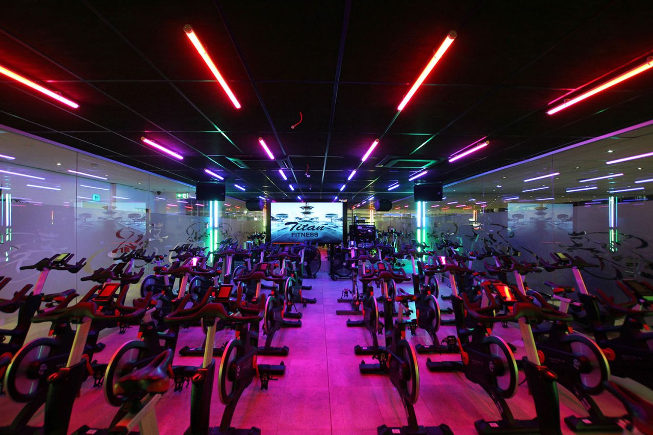Red and purple light tubes above rows of bikes at Titan Fitness Sydney.