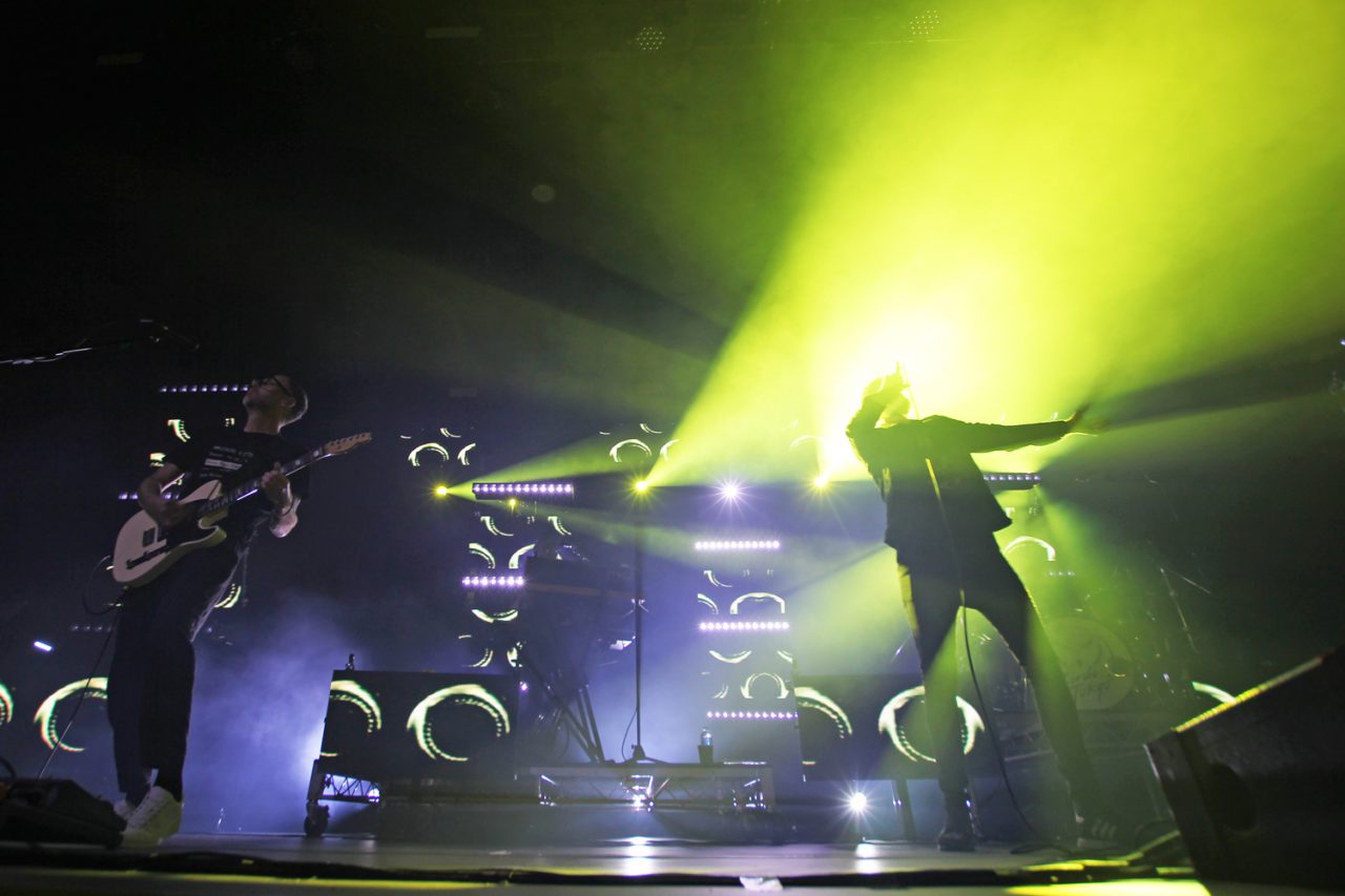 Band members silhouetted against bright green stage lighting.