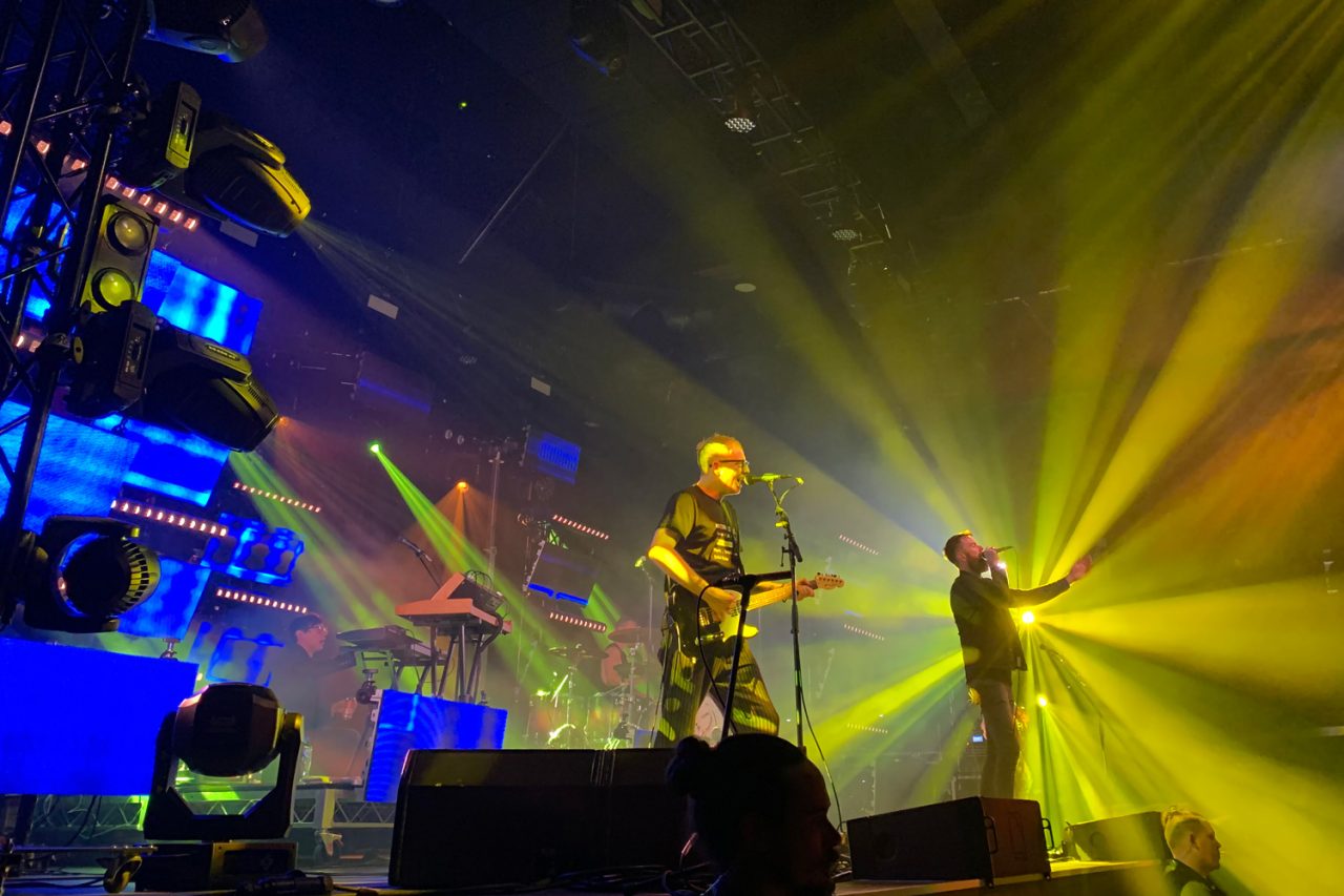 Birds of Tokyo performing beneath yellow beams.