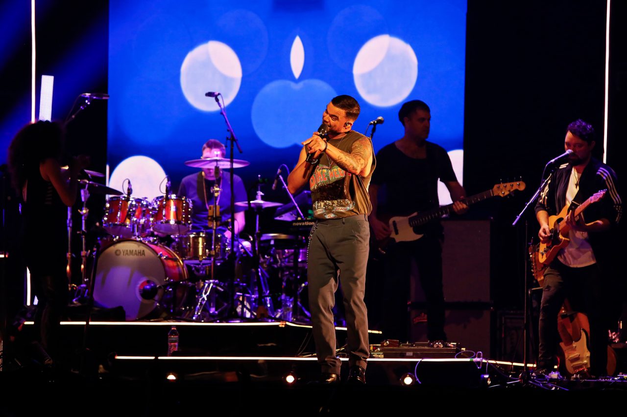 Vocalist and band perform in front of blue video graphics on the Ridin' With You tour.